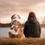 Woman and dog sitting at water's edge