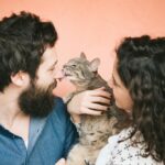 Cat in woman's arms licking man's nose