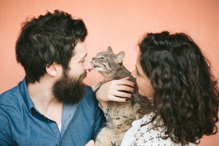 Cat in woman's arms licking man's nose