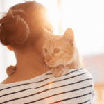 Woman holding cat on her shoulder.